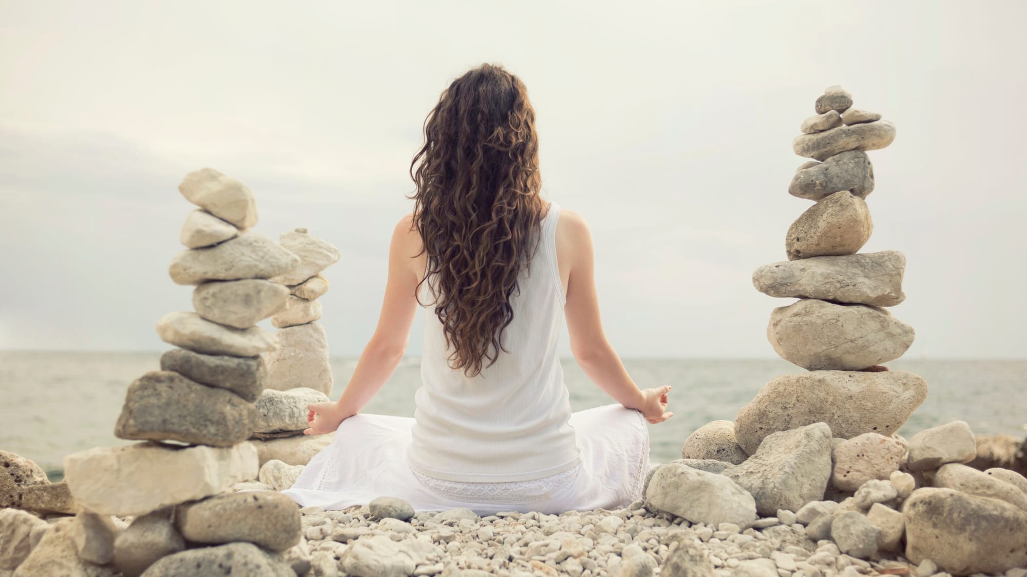 woman meditating on the beach with balance stones - The witch wound - SageSistas